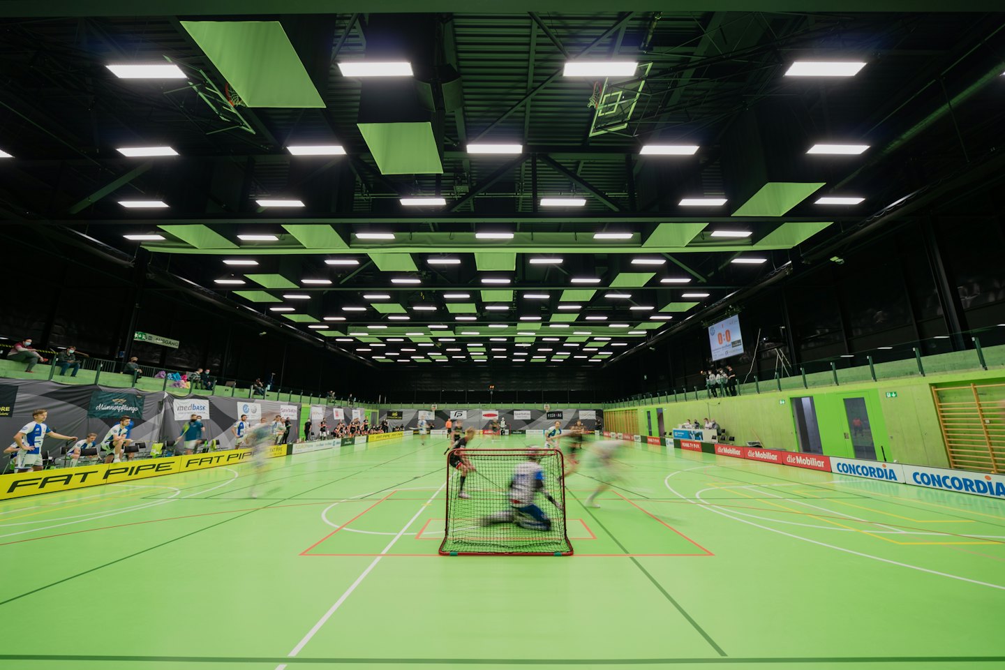 Giocatori di floorball circondano un portiere in una partita indoor frenetica.