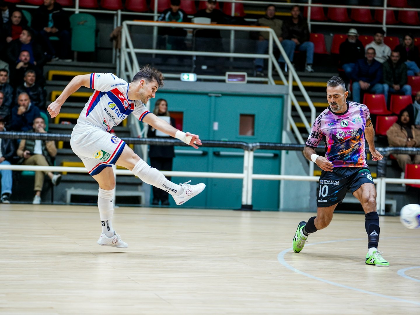 Due uomini si contendono un pallone da calcio su un campo indoor.