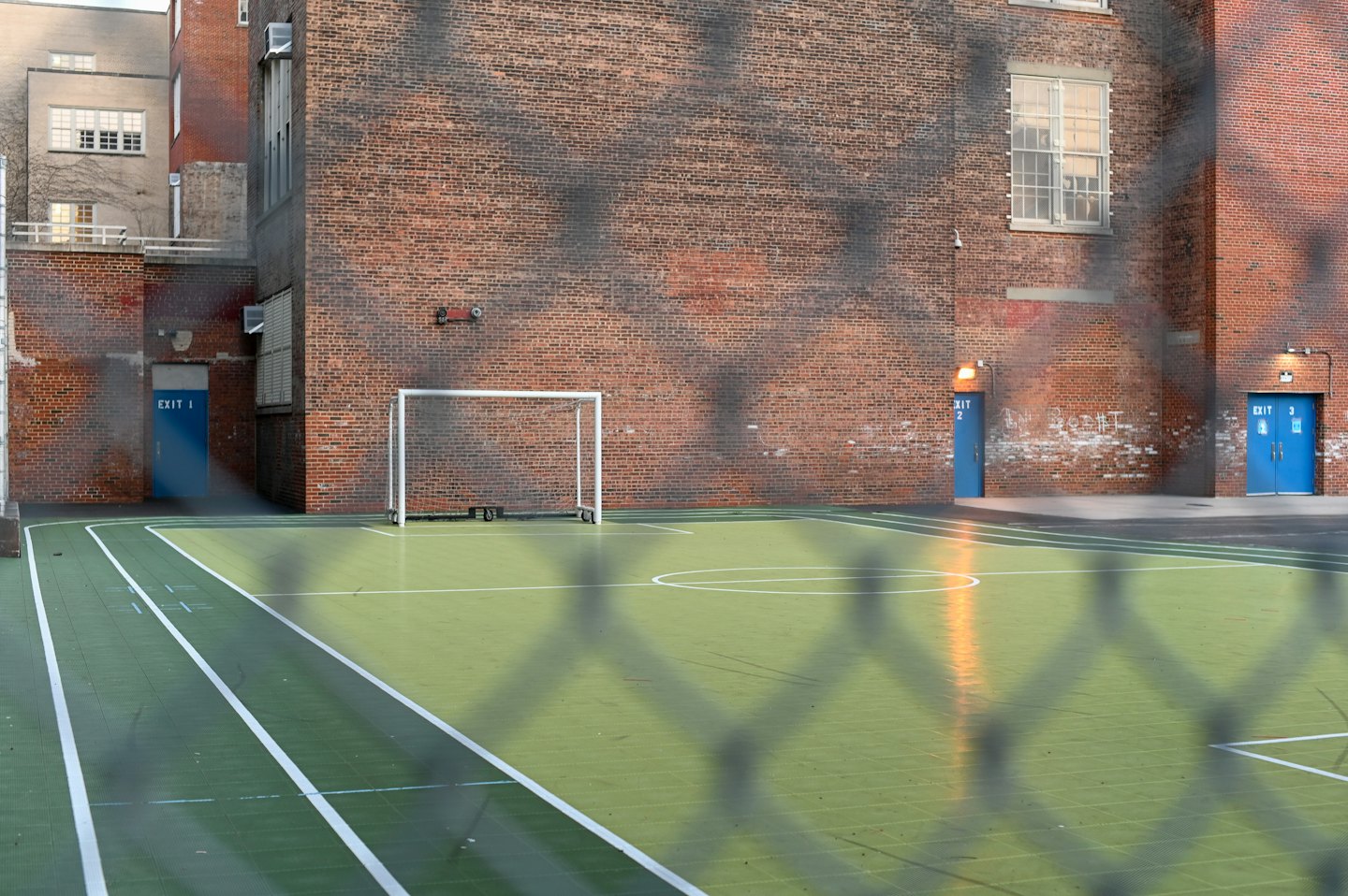 Porta da calcio su campo sportivo vista attraverso rete metallica.