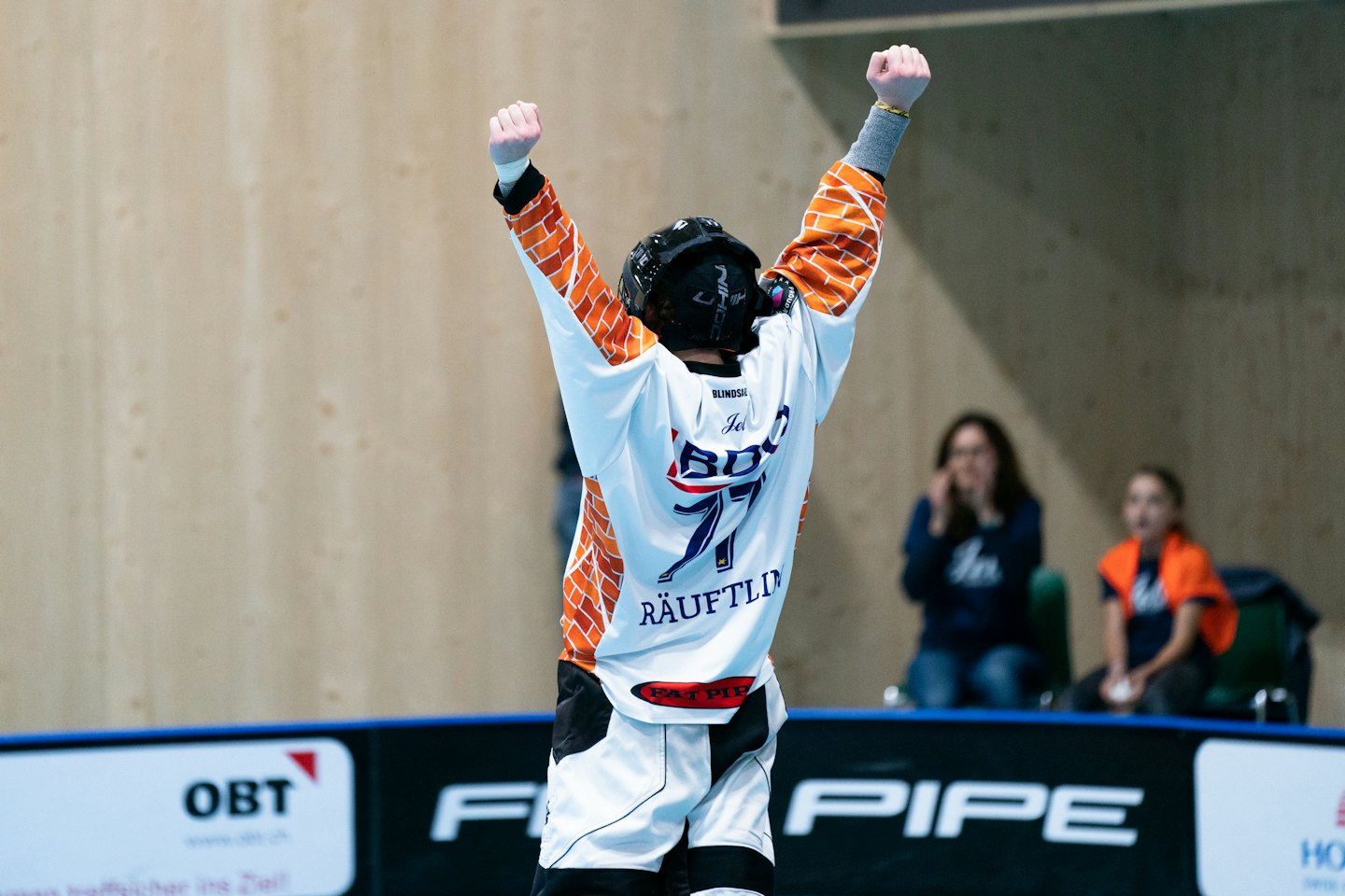 Giocatore di floorball in maglia bianca, arancione e nera festeggia la vittoria.