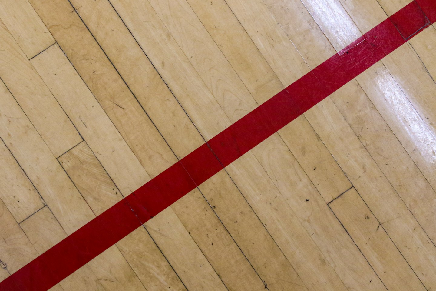 Una linea rossa dipinta divide un campo sportivo in legno usurato.